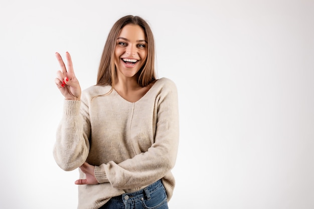 Femme souriante et montrant deux doigts comme geste de paix isolé sur blanc