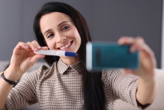 Femme souriante montre un test de grossesse sur smartphone. Comment parler à votre partenaire du concept de grossesse