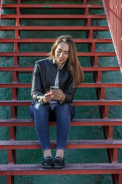 Une femme souriante navigue sur son smartphone dans les escaliers.