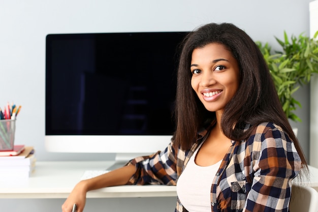 Femme souriante noire assise sur le lieu de travail en regardant la caméra