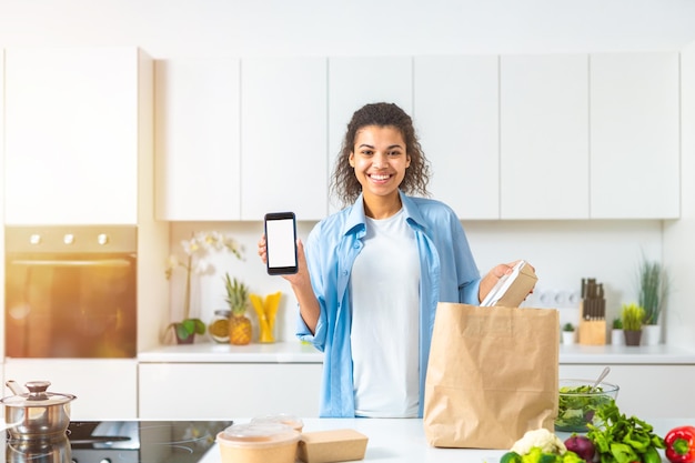 Femme souriante avec un panier commandé en ligne via smartphone et livré directement à domicile