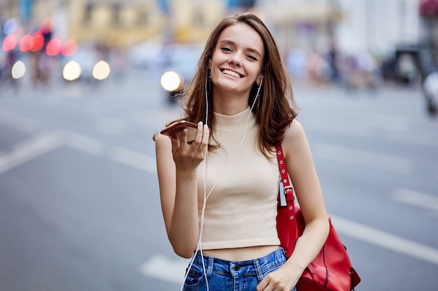 Femme souriante parle par smartphone dans la rue près de la circulation