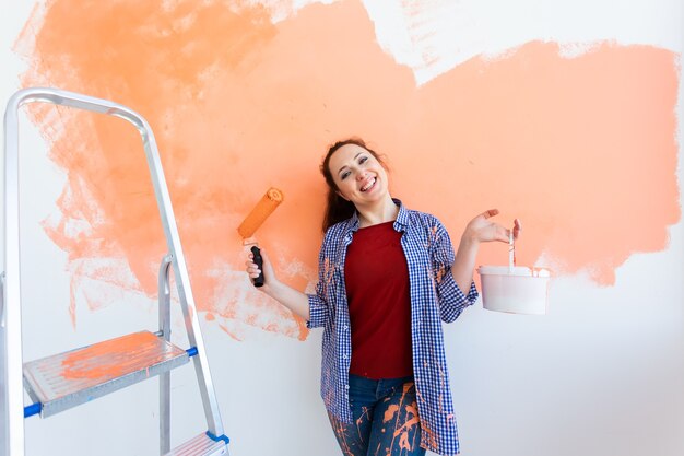 Femme souriante peinture mur intérieur de la maison. Concept de rénovation, réparation et redécoration.