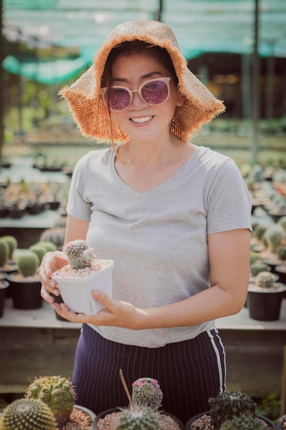 Femme souriante à pleines dents avec bonheur tenant un pot de cactus mamillaria à la main