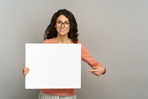 Une femme souriante avec un point d'affiche vide vers une affiche vierge affiche une publicité sur un panneau ou une bannière