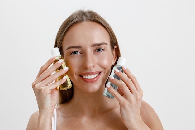 Photo femme souriante portant de la lingerie tenant des bouteilles avec des produits cosmétiques de soin de la peau sur fond de studio