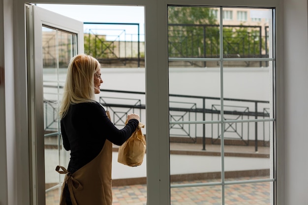 Femme souriante portant un tablier avec des sacs en papier à l'extérieur