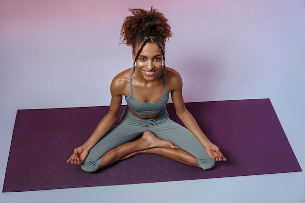 Femme souriante pratiquant le yoga et la méditation sur tapis sur fond de studio avec filtre de couleur