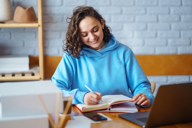 Une femme souriante prend des notes sur les commandes avec un ordinateur portable Le propriétaire de Dropshipping travaille