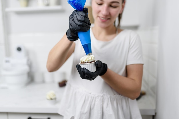 Une femme souriante presse la crème d'une seringue à pâtisserie sur un muffin