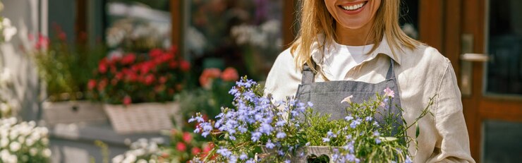 Une femme souriante, propriétaire d'une entreprise de fleuristerie, debout avec une plante d'intérieur sur le fond d'un magasin de fleurs