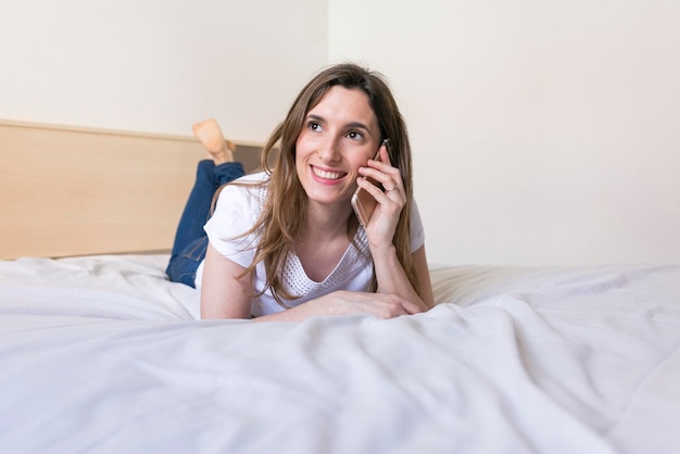 Une femme souriante qui utilise son téléphone alors qu'elle est allongée sur le lit à la maison