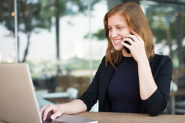 Femme souriante regardant ordinateur portable et parler au téléphone