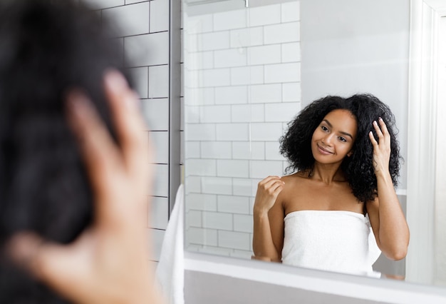 Une femme souriante regardant son reflet dans un miroir et ajustant ses cheveux