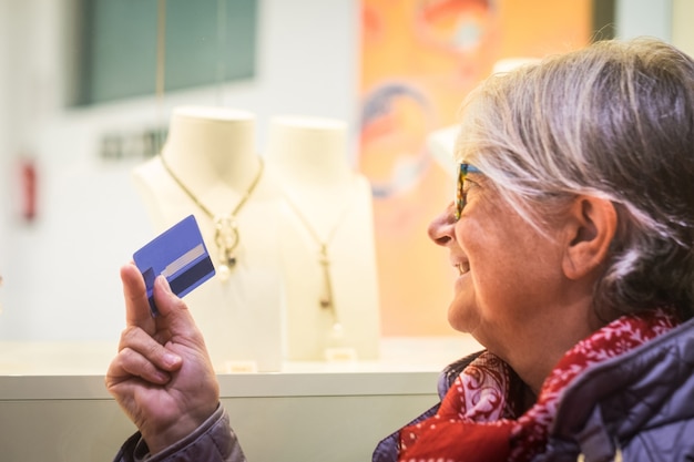 Une femme souriante regarde les fenêtres illuminées affichant des bijoux avec la carte de crédit en main