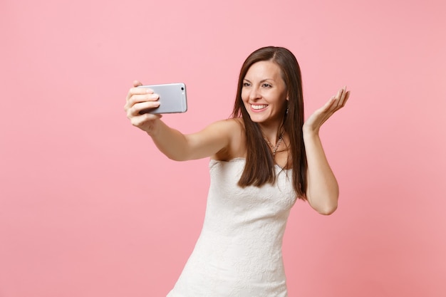 Femme souriante en robe blanche écartant les mains, prenant une photo de selfie sur un téléphone portable ou passant un appel vidéo