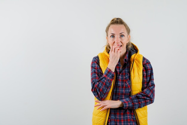 La femme souriante ronge ses ongles sur fond blanc