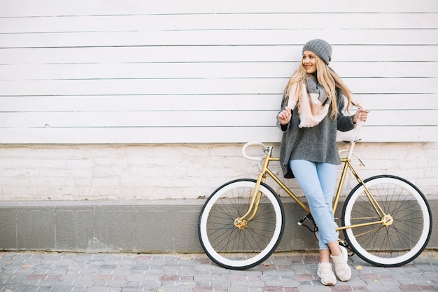 Femme souriante s'appuyant sur bicyclette près du mur