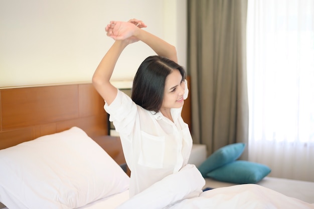 Une femme souriante s'étendant les mains après s'être réveillé le matin à la maison.
