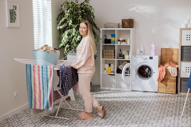 Une femme souriante se tient dans la salle de bains de la buanderie par un sèche-linge tire lavé propre sentant