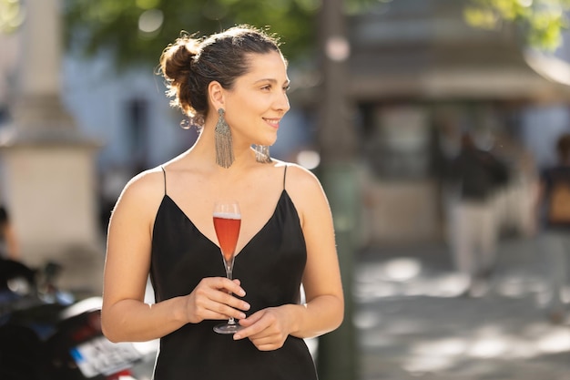 Femme souriante à une soirée décontractée en robe élégante tenant un verre et regardant sur le côté