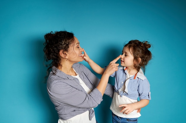 Femme souriante et son enfant se touchant le nez sur une surface bleue avec copie espace