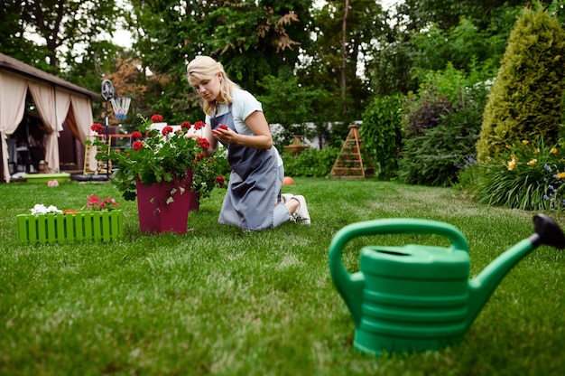 Femme souriante en tablier travaille avec des fleurs dans le jardin