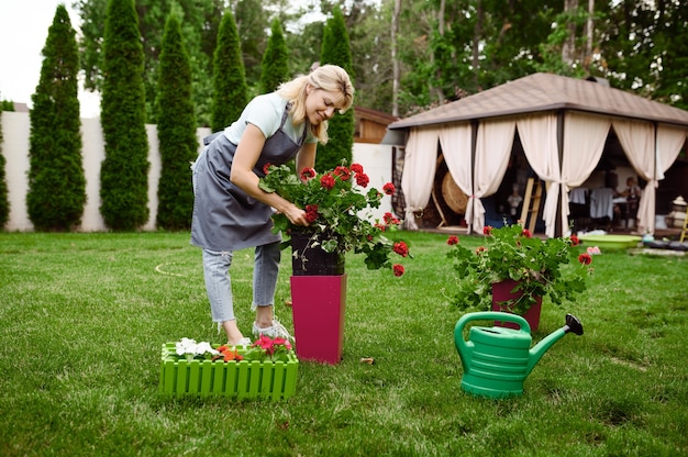 Femme souriante en tablier travaille avec des fleurs dans le jardin