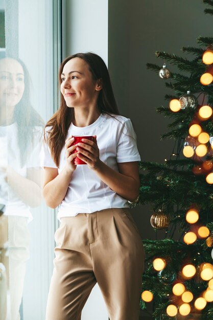 Femme souriante avec une tasse près du sapin de Noël