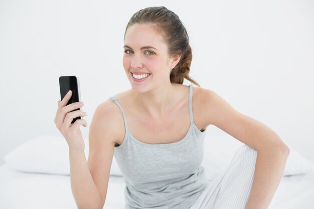 Femme souriante avec téléphone portable assis dans son lit