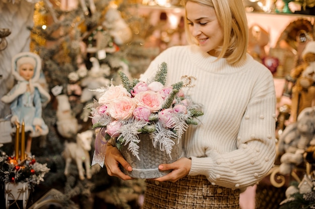 Femme souriante tenant une boîte à motif pull gris avec des roses de pivoine rose clair décorées de branches de sapin