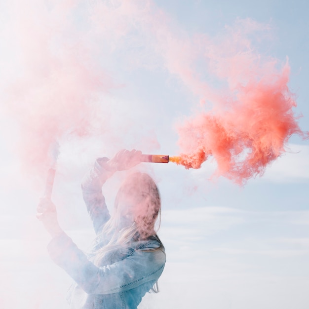 Femme souriante tenant des bombes de fumée rouge