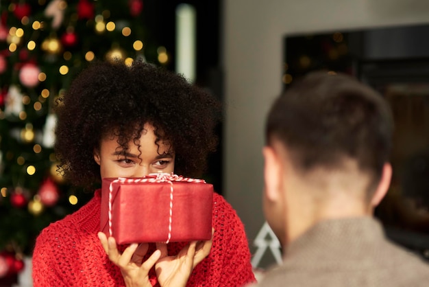 Photo une femme souriante tenant un cadeau de noël devant un homme à la maison.