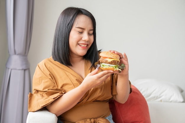 femme souriante et tenant hamburger et assis dans le salon