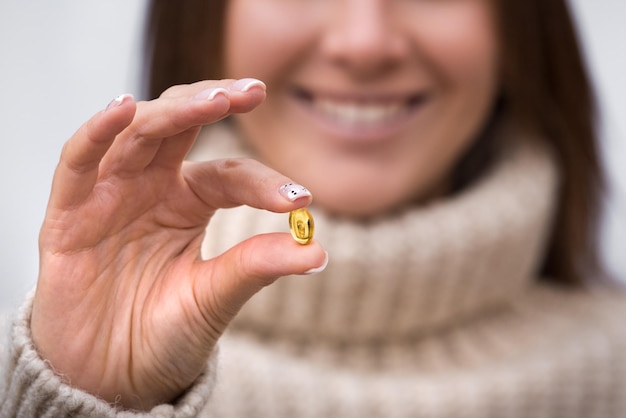 Photo femme souriante tenant une pilule d'huile de poisson ou un supplément de vitamine d capsule avec oméga 3