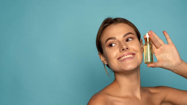 Femme souriante tenant un sérum de vitamine c près de son visage sur fond bleu. Concept de soins de la peau et de santé. Bannière Web.