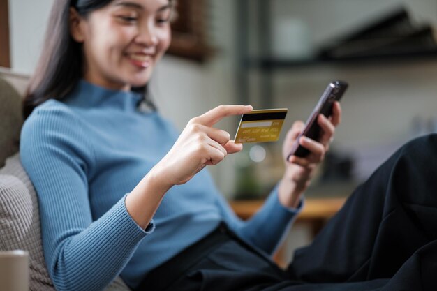 Une femme souriante tenant un smartphone et une carte de crédit bancaire impliquée dans des achats mobiles en ligne à la maison une femme acheteuse heureuse achetant des biens ou des services dans un magasin en ligne