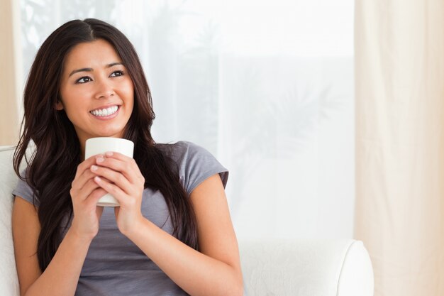 femme souriante tenant une tasse en regardant le plafond