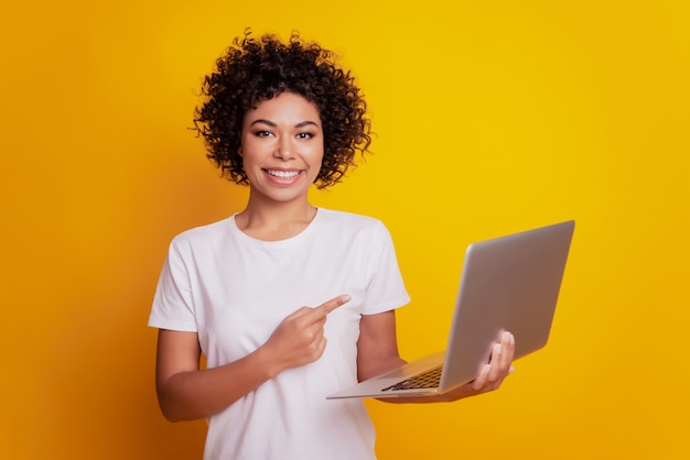 Photo femme souriante tenir le doigt direct de l'ordinateur portable faisant la promotion sur le mur jaune