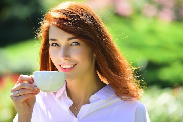 Femme souriante à tête rouge tasse de café en gros plan portrait de belle jeune femme tenant la tasse de mor...