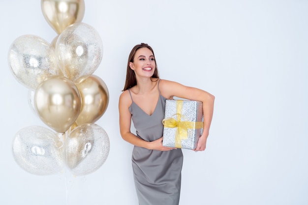 Une femme souriante tient une grande boîte-cadeau emballée près des montgolfières venues célébrer la fête