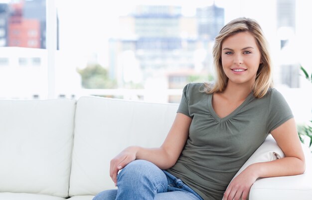 Femme souriante tout en étant assis sur le canapé avec les jambes croisées