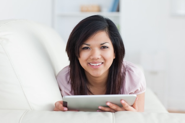 Femme souriante tout en se reposant sur un canapé et en jouant avec une tablette