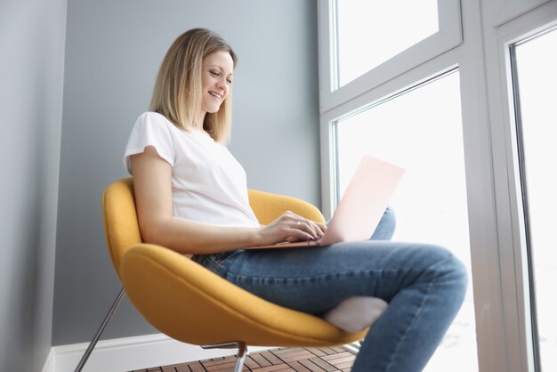 Femme Souriante Travaillant Sur Ordinateur Portable Alors Qu'il était Assis Dans Une Chaise