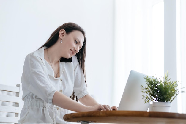 Femme souriante travaillant sur un ordinateur portable et parlant sur son smartphone