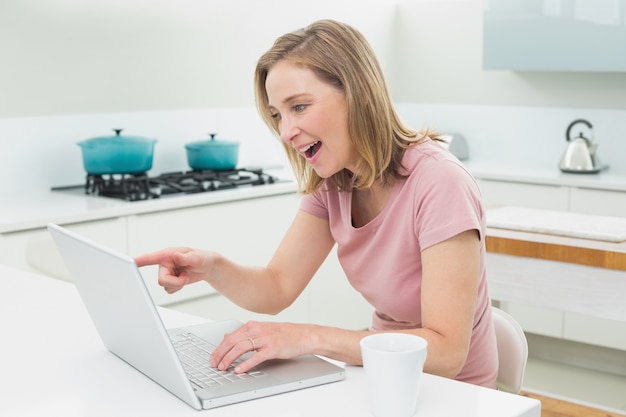 Femme souriante utilisant un ordinateur portable dans la cuisine