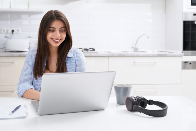 Femme souriante utilisant un ordinateur portable à la maison dans la cuisine