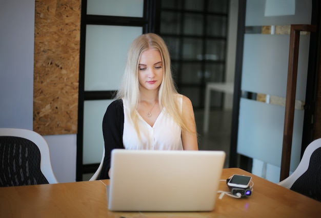 Une femme souriante utilisant un ordinateur portable sur son lieu de travail pour les petites entreprises cherchant à engager le public et à faire évoluer la création de contenu peut adopter une nouvelle technologie de marketing dans l'espace de travail. Notion de pigiste.