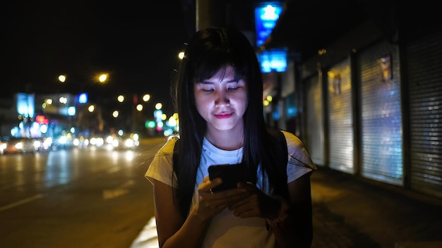 Photo une femme souriante utilisant un téléphone intelligent debout sur la route la nuit