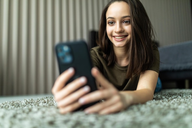 Femme souriante utilisant un téléphone portable alors qu'elle était assise sur le sol à la maison